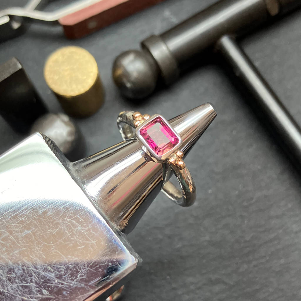 Silver ring with a pink gemstone oAmanda Cox's workbench with jewellery tools. Heart Gallery