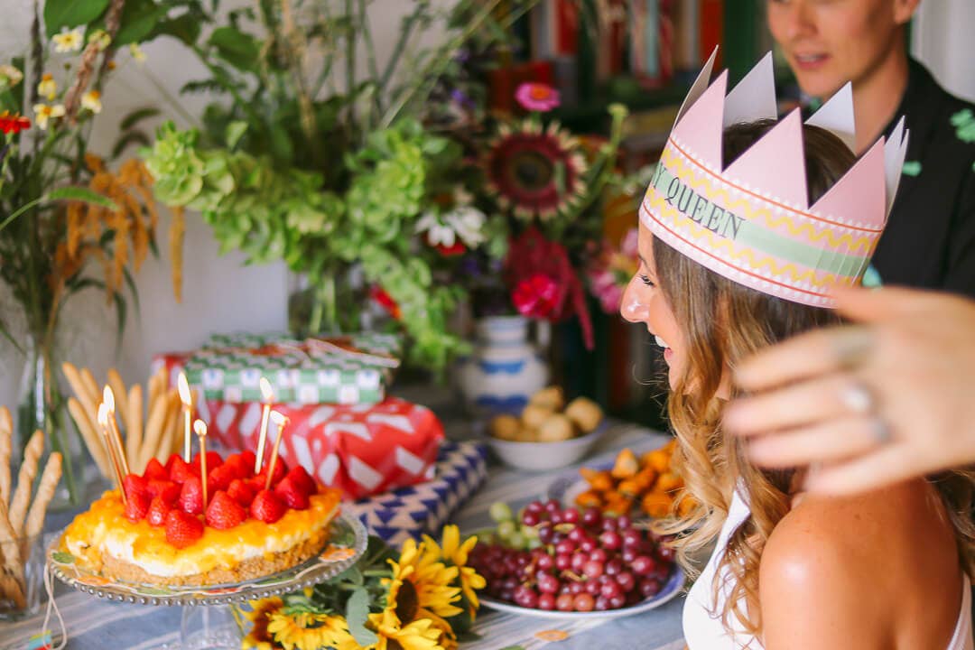 Person wearing a 'Queen' paper crown at a festive table with food and decorations.