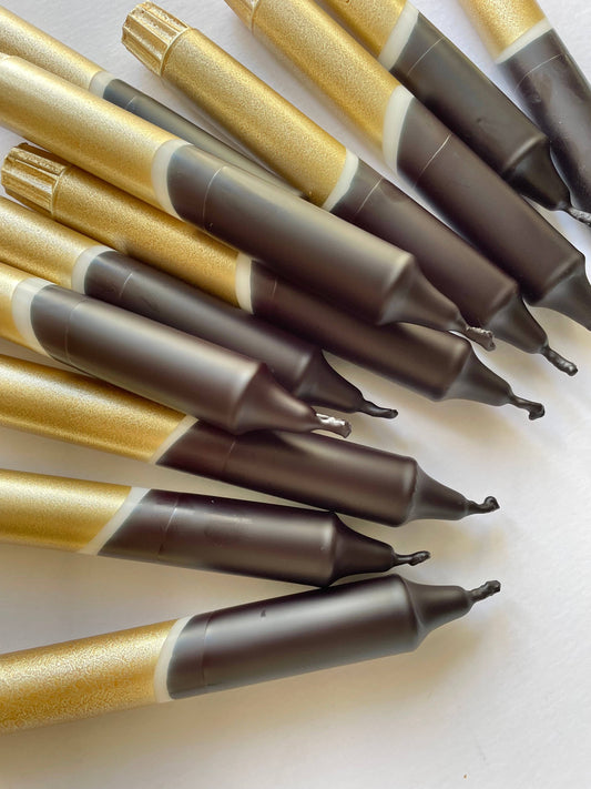 A group of black and gold dip dyed dinner candles with varying lengths, displayed on a white surface by The Singing Rabbit
