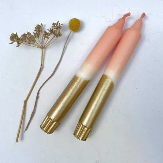 Two dinner candles with a blush pink and gold color scheme, displayed alongside some decorative dried flowers.