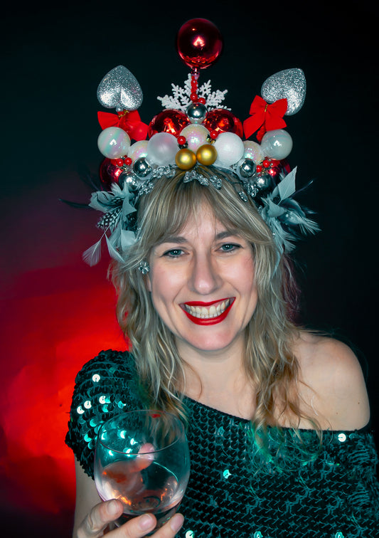 Woman wearing a festive headpiece with red, silver, and gold decorations, holding a glass of wine ready for our Christmas Crowns and Conversations event at Heart Gallery