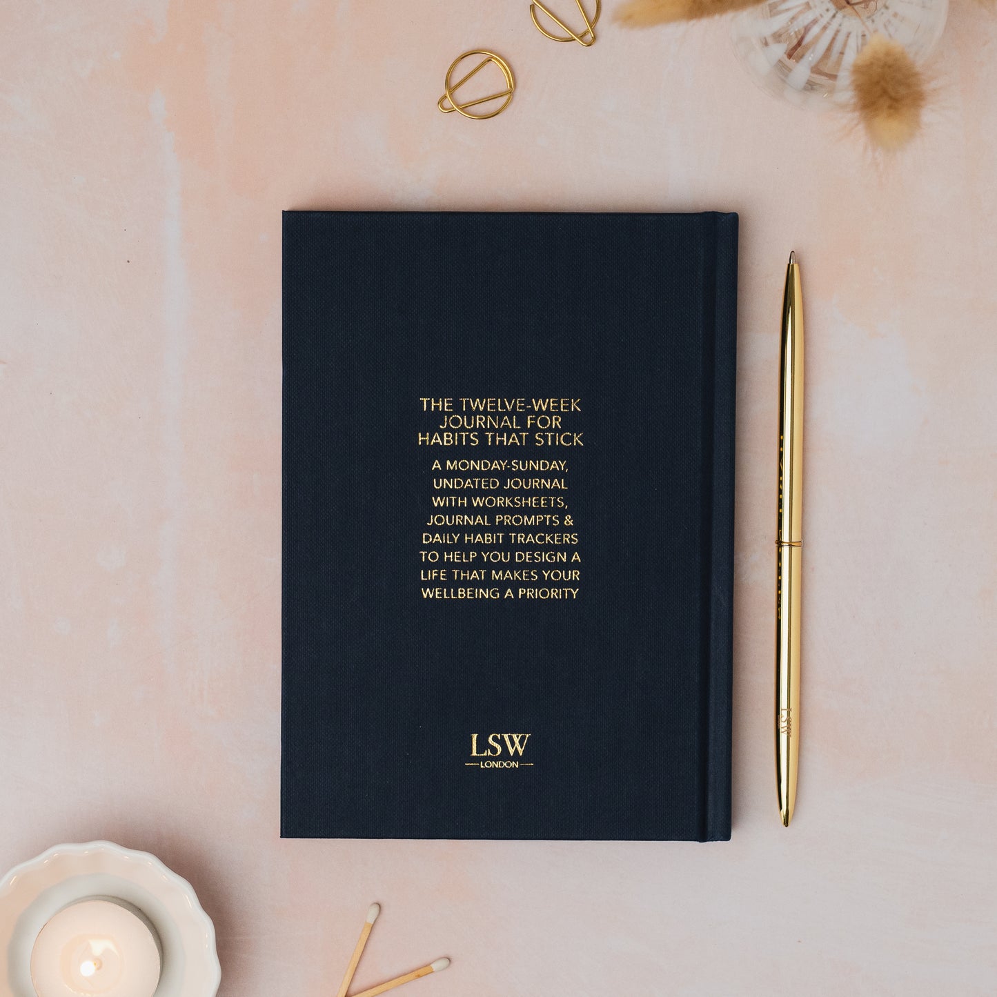 Dark blue journal with gold text on a light pink surface with decorative items12 week journal by LSW