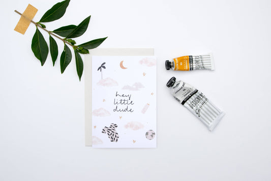 Card with 'hey little dude' text, paint tubes, and a branch on a white background