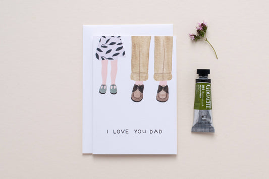 Greeting card with illustration of a child and adult, 'I Love You Dad', next to a paint tube on a beige background
