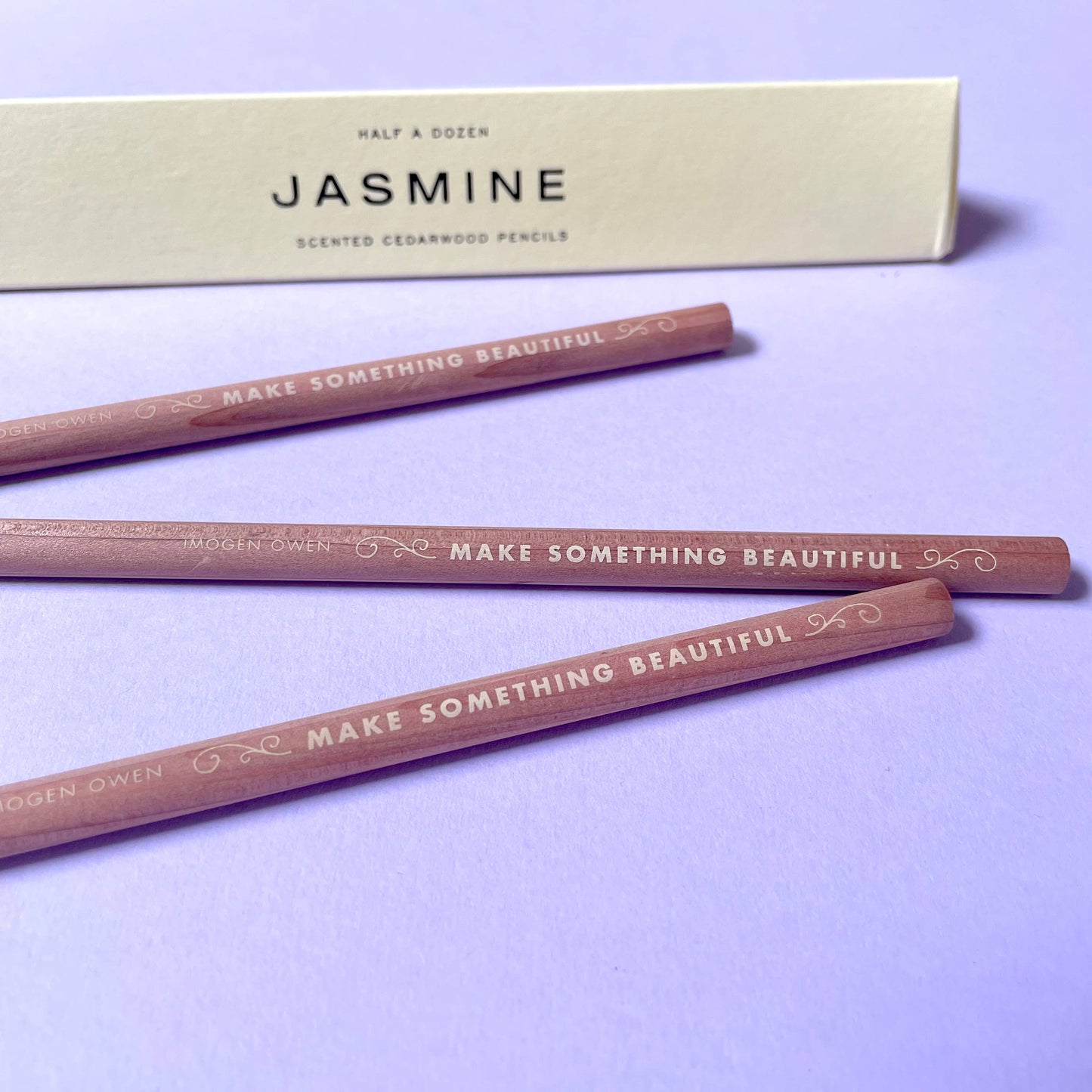 half a dozen scented cedarwood pencils with 'Make Something Beautiful' text on a purple background, accompanied by a letterpress box labeled 'Jasmine' by Imogen Owen for Heart Gallery