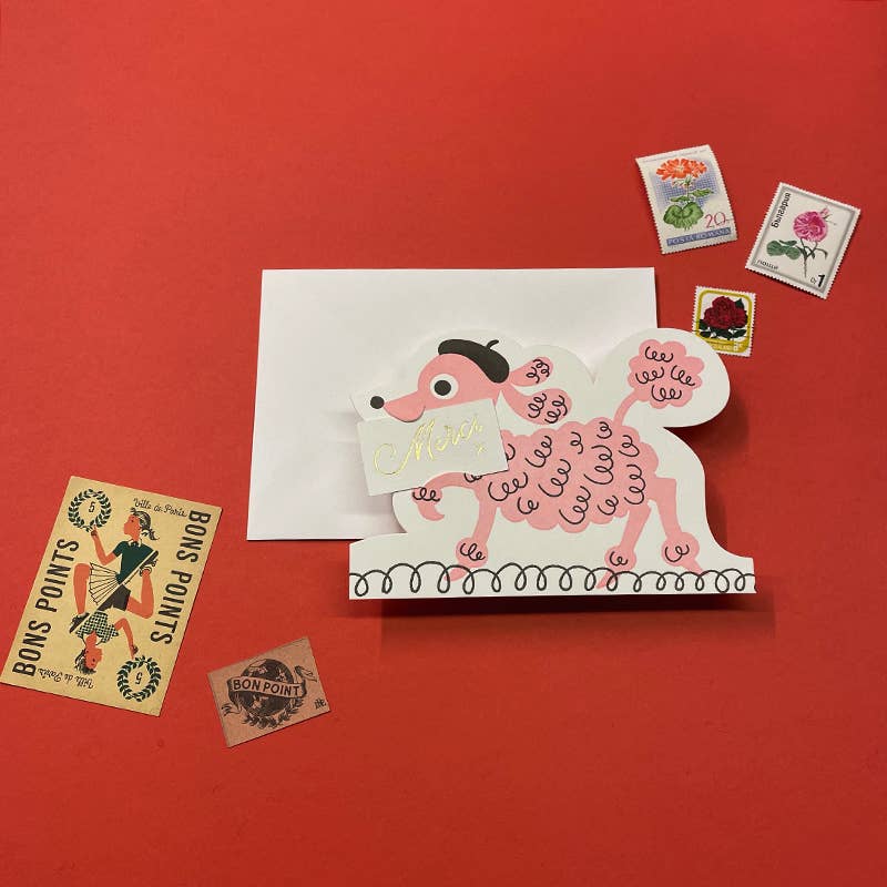 Card with a pink poodle carrying a Merci sign in its mouth on a red background