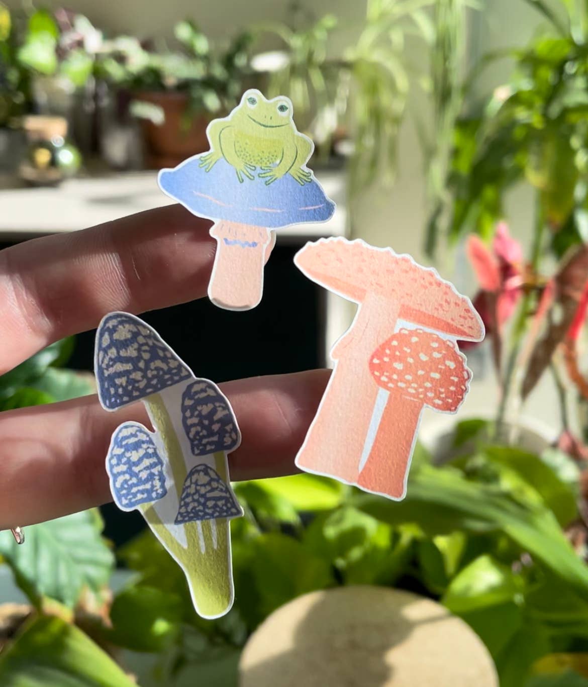 Mushroom stickers by Another Studio on fingers on a green background