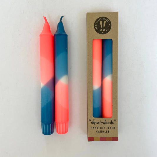 Two hand-dip-dyed candles in neon coral and teal blue with their packaging on a white background by The Singing Rabbit