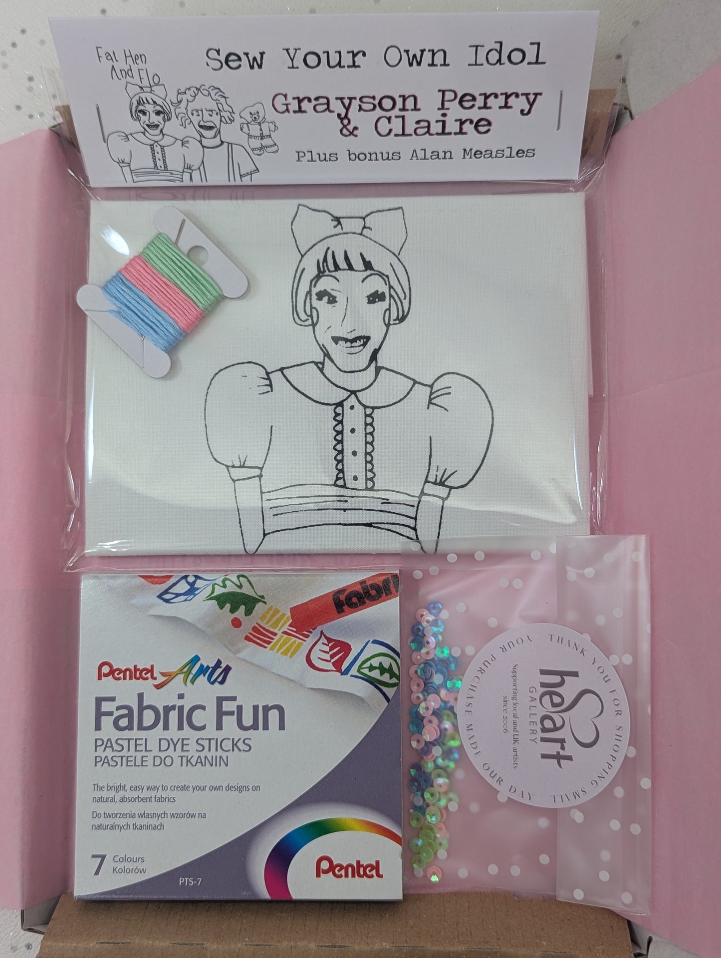 Craft kit with coloring book, fabric fun sticks, and other supplies on a pink background Grayson Perry and Claire