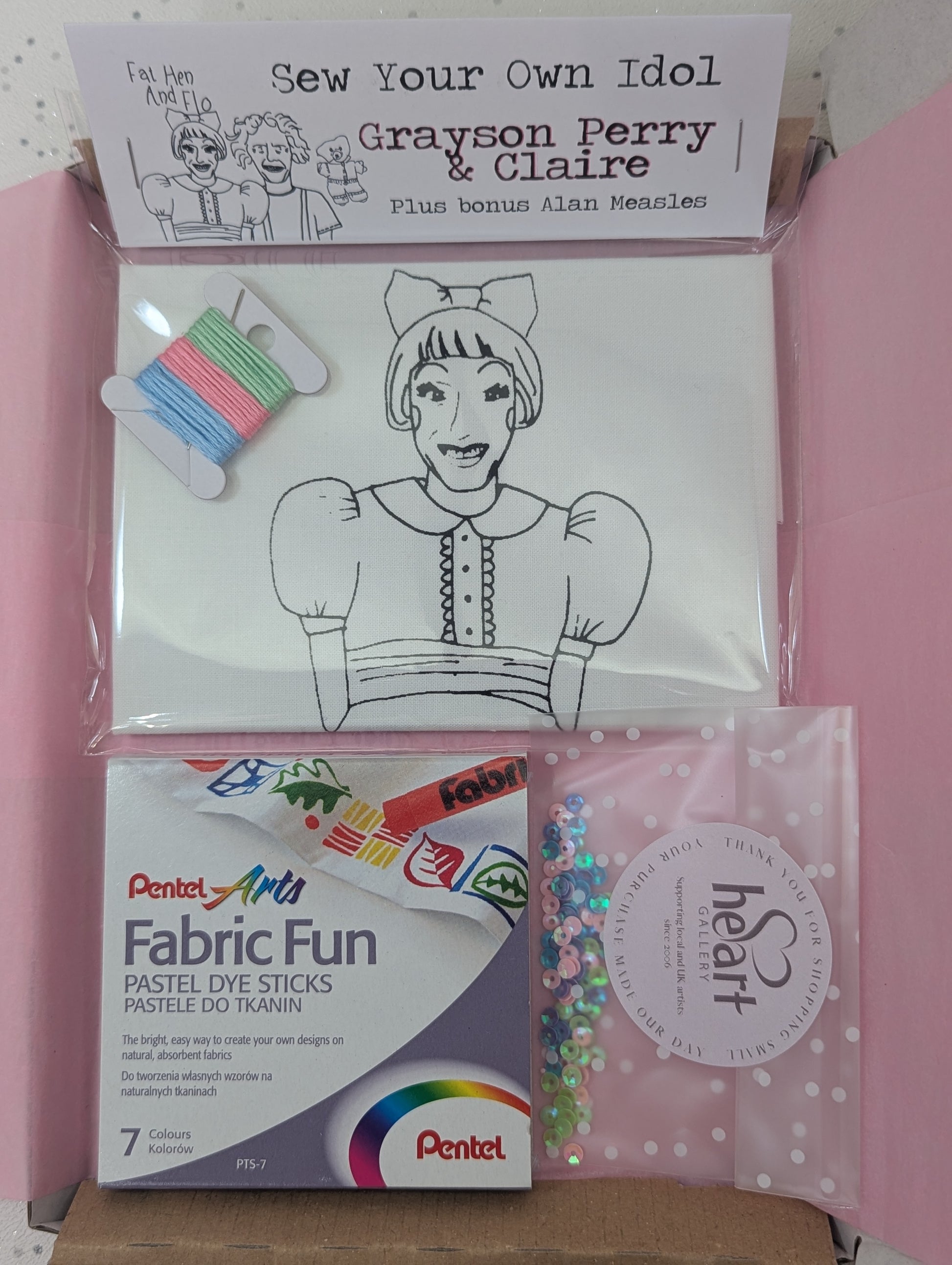 Craft kit with coloring book, fabric fun sticks, and other supplies on a pink background Grayson Perry and Claire