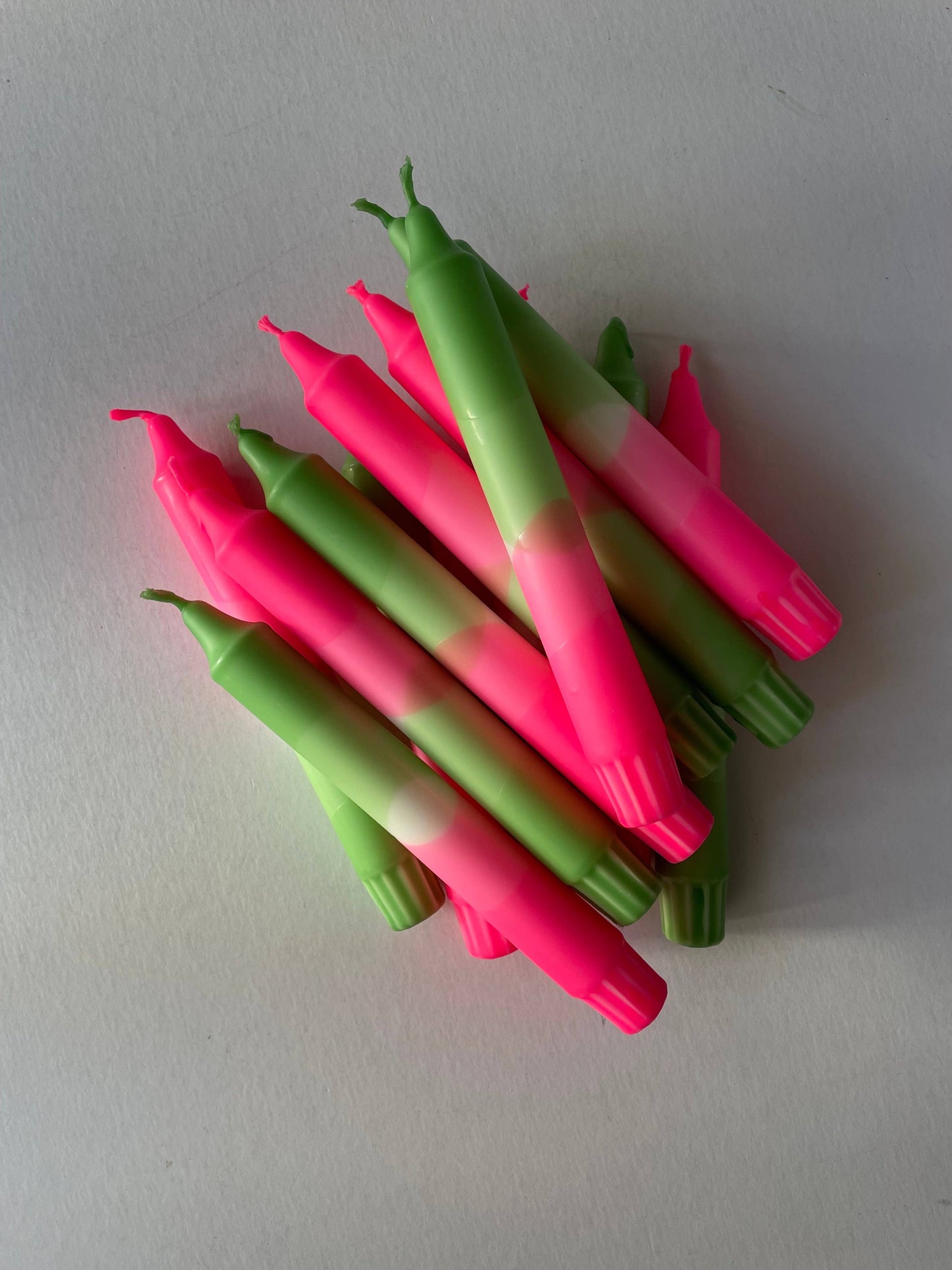 Pink and green candles stacked on a white surface by The Singing Rabbit