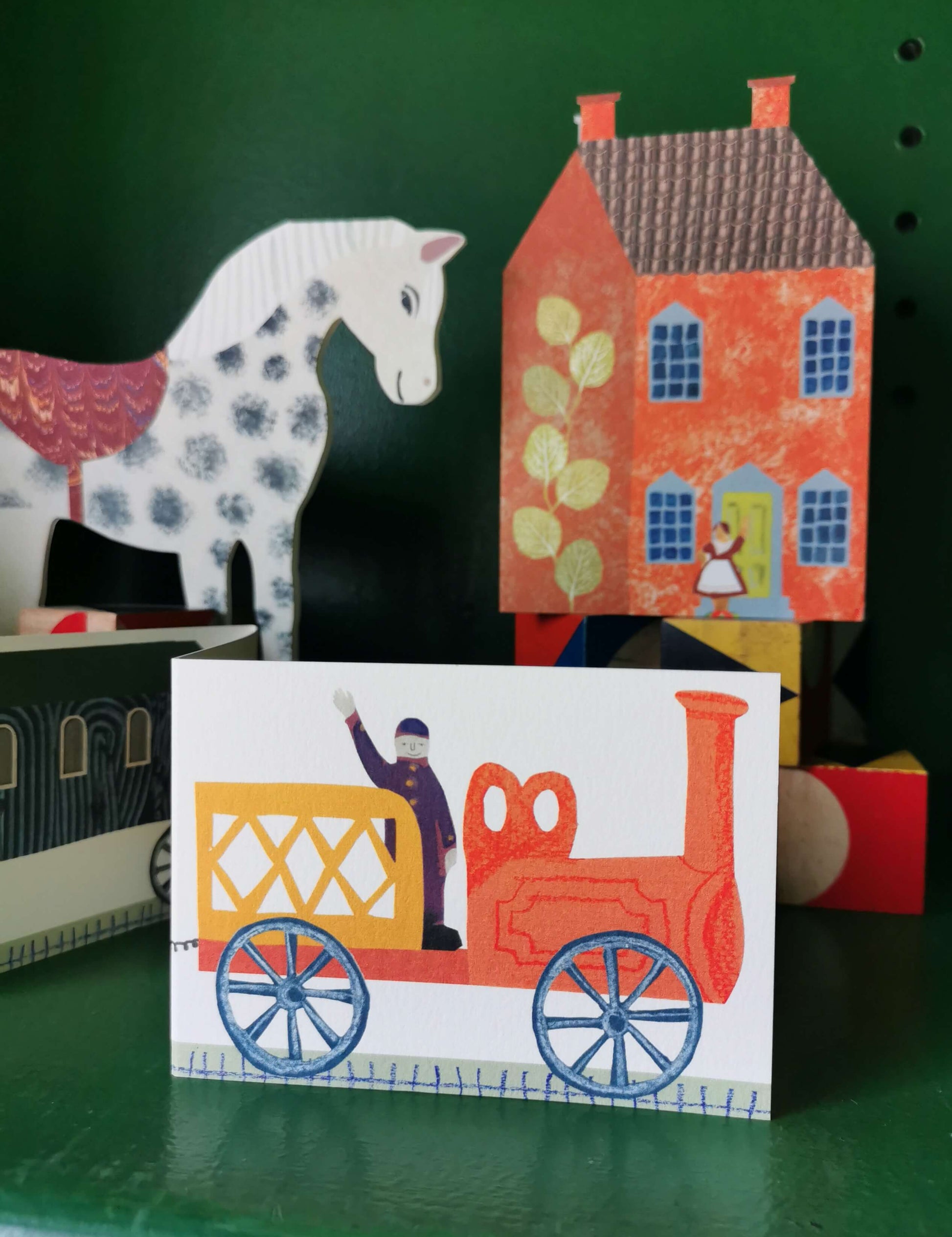 Colorful paper toy set with a horse, house, and train on a green surface.