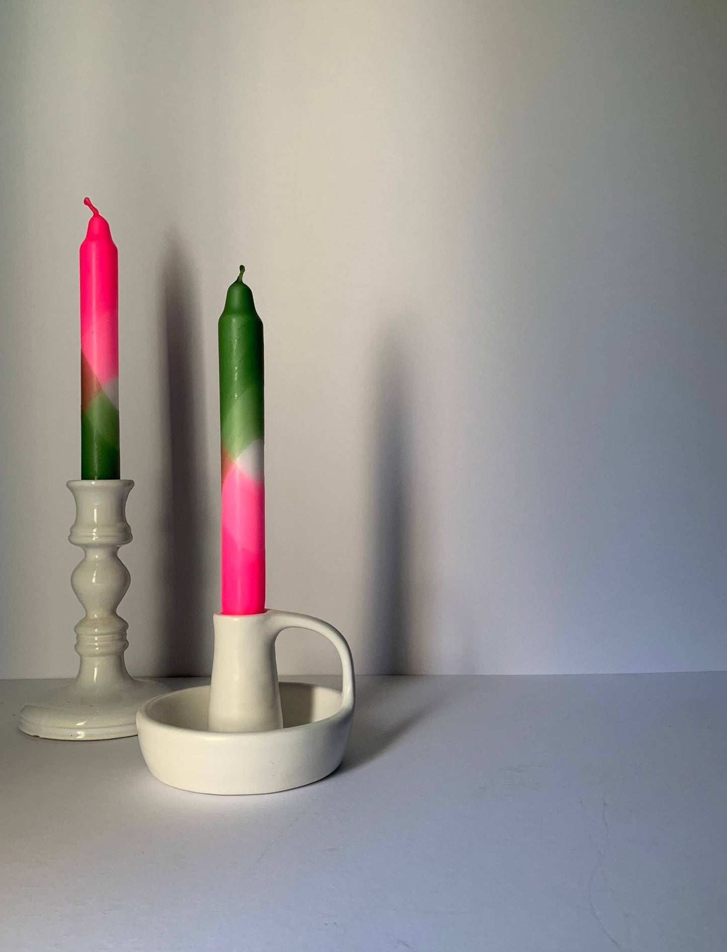 Two candles with pink and green gradient in a white holder on a plain background by The Singing Rabbit