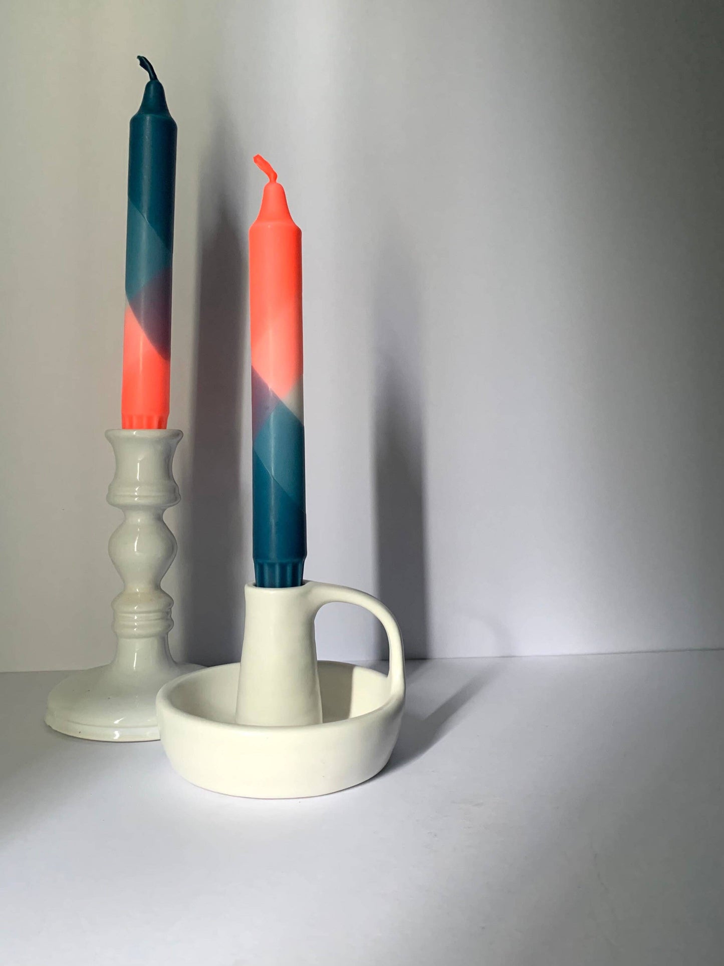 Two colorful candles in a white candle holder on a plain background by The Singing Rabbit