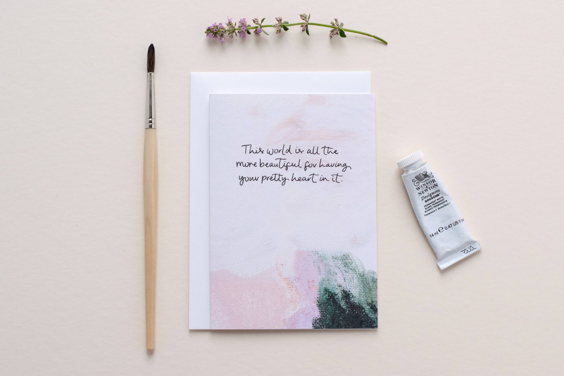 card with a motivational quote, paintbrush, and tube of paint on a light background