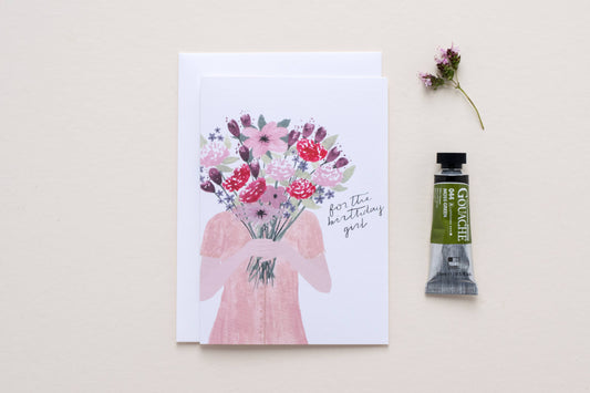 Gouache paint tube next to a greeting card with floral design and text on a light background birthday girl card