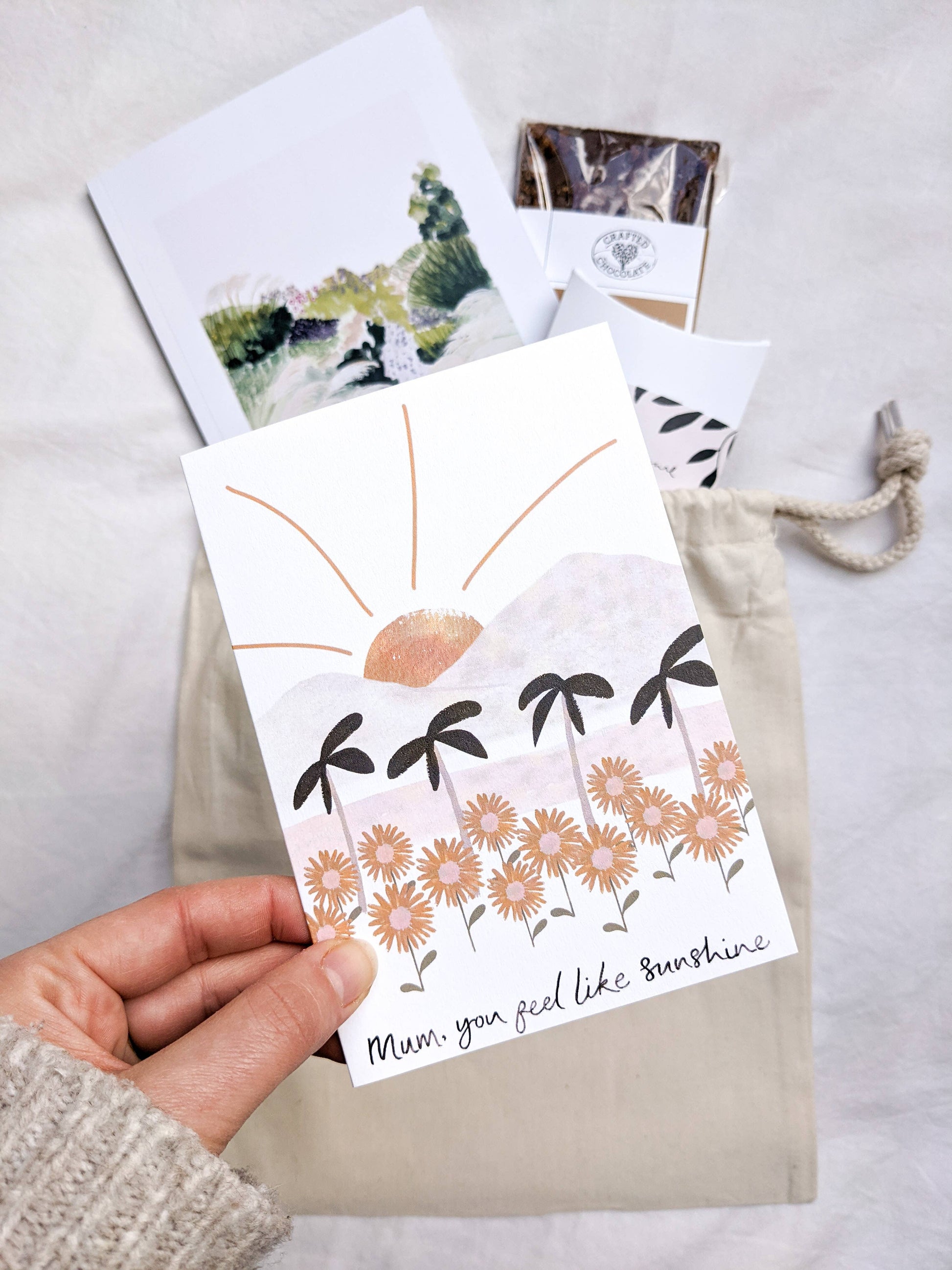 Hand holding a card with floral design and text, with other cards and a drawstring bag in the background.