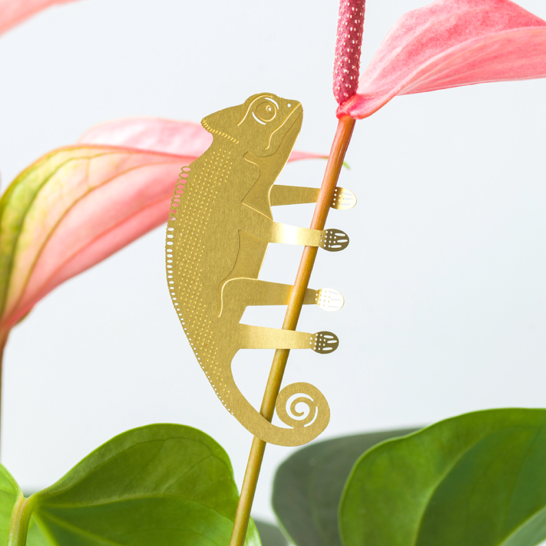 Gold chameleon-shaped decorative item on a pink flower with green leaves.