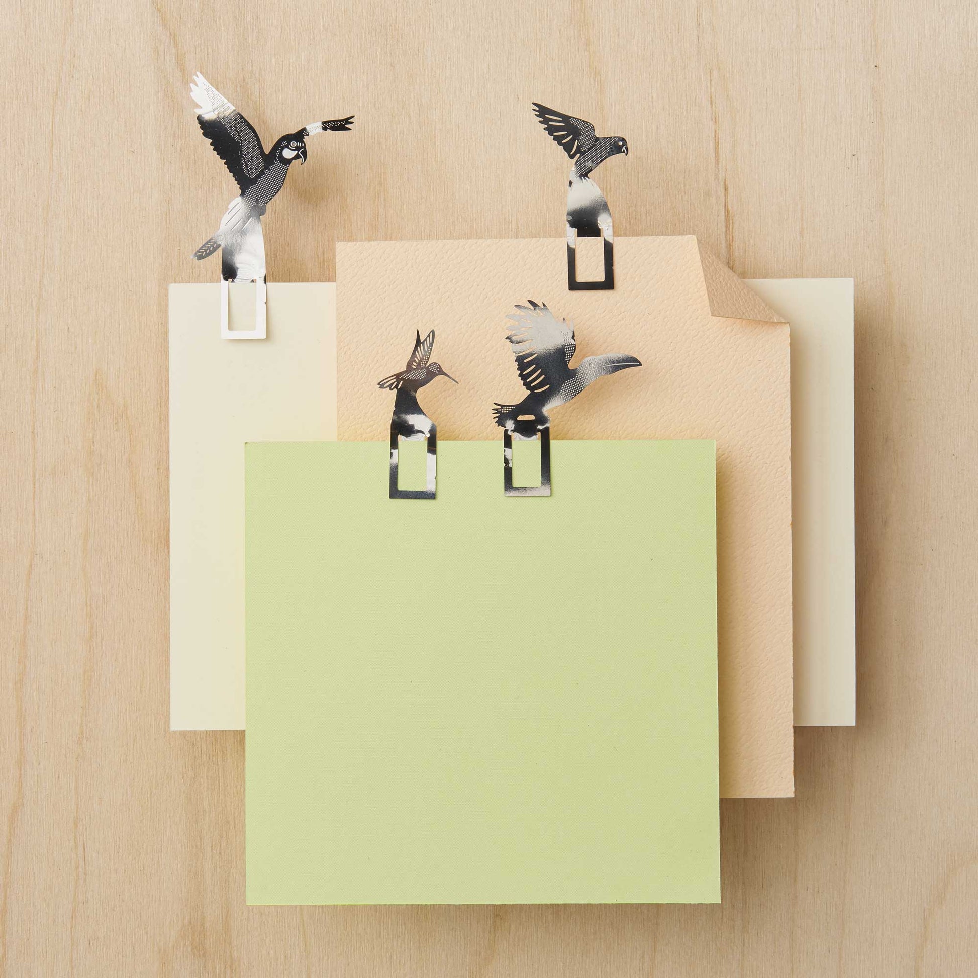 Bird-shaped paper clips on a stack of colored papers on a wooden surface