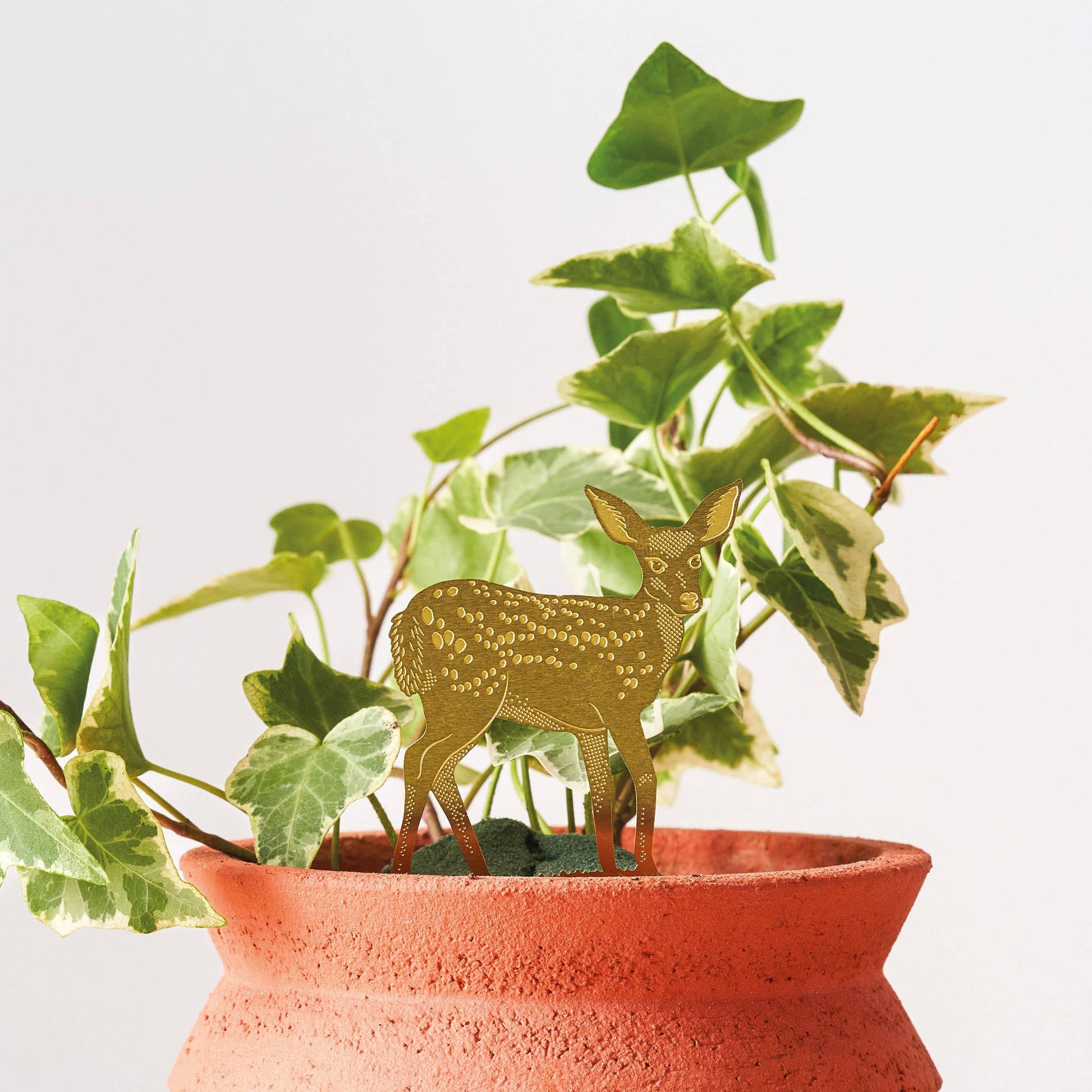 A brass deer decoration placed on a plant pot, with green leaves in the background.