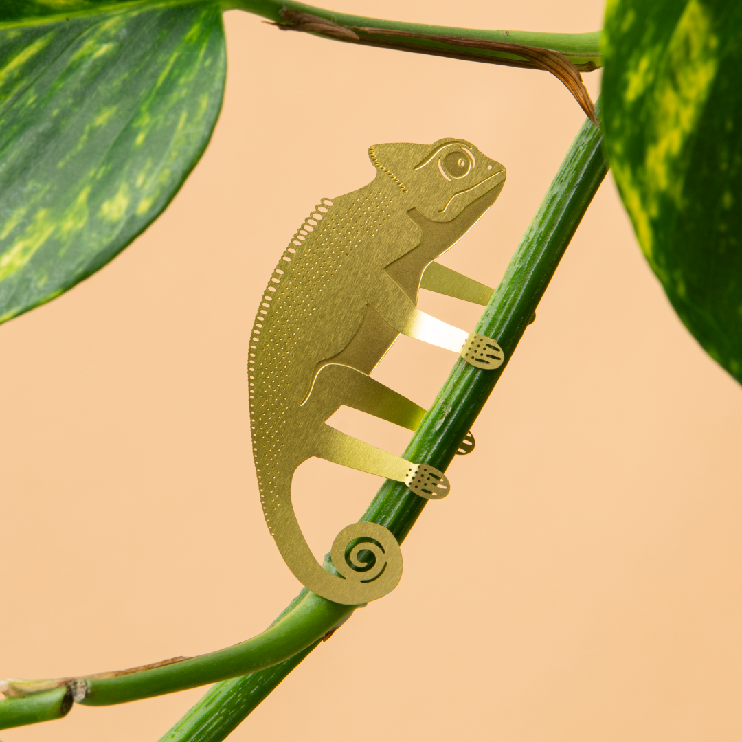Metallic green chameleon sculpture on a branch with a beige background