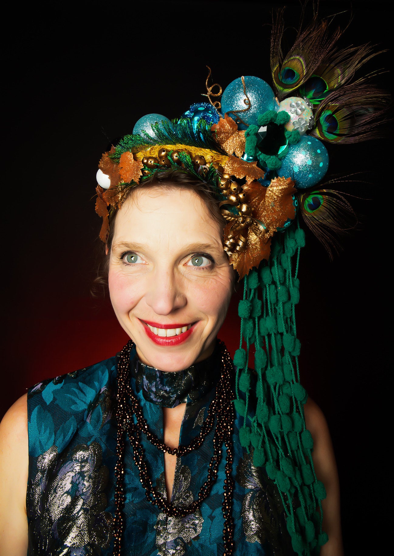 Lisa wearing a decorative headpiece with peacock feathers and beads against a black background for our Christmas Crowns and Conversations Event