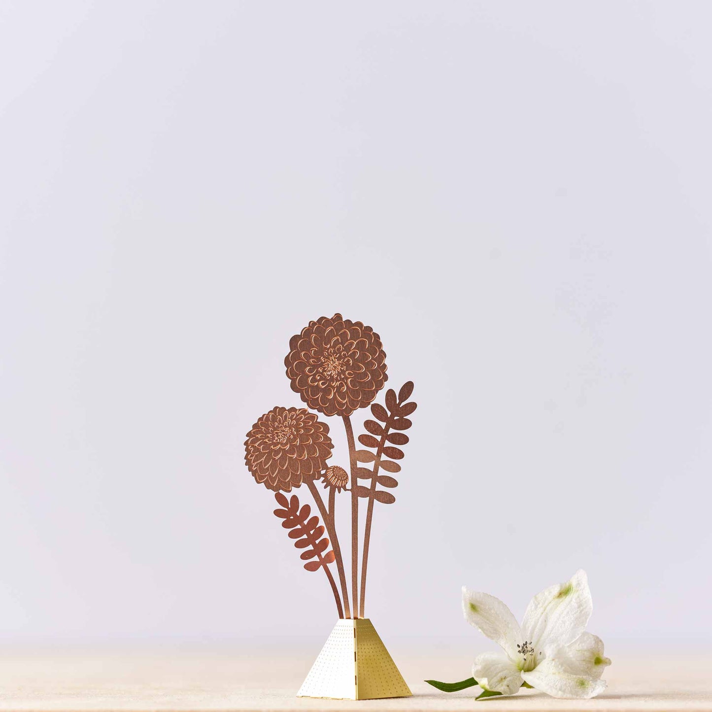 tiny dahlial bouquet vase decoration by Another Studio made of brass with a gold finish, with a base and three-dimensional flowers, against a blue background.