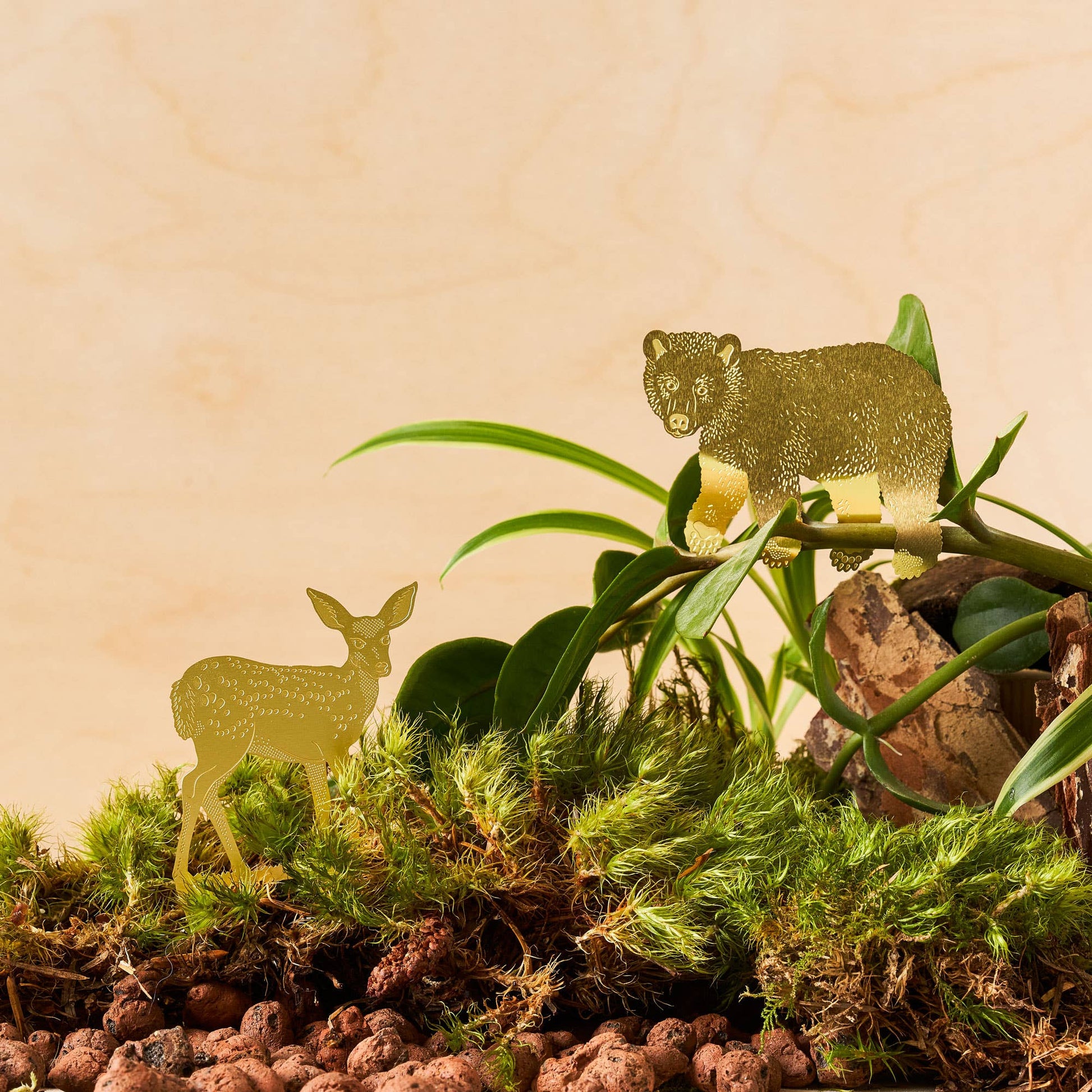 A brass deer decoration placed on a plant pot, with green leaves in the background by Another Studio