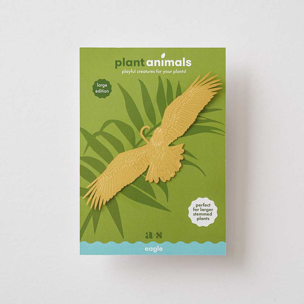 A gold-colored brass plant animal in the shape of an eagle, with open wings, positioned among green plant leaves by Another Studio for Heart Gallery