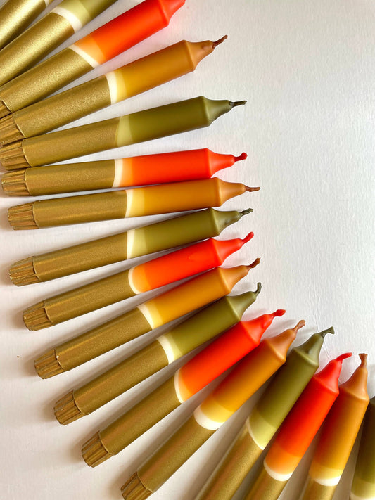 A set of 3 dinner candles with a dip-dyed design, transitioning in colors from olive green to caramel, rust, and gold, arranged in a semi-circle on a light background.