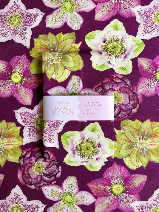 A multicolored floral tea towel with a prominent purple hue and green leaves, featuring a label with the brand name 'Freya Snow'.