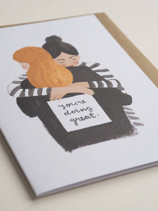 Greeting card with illustration of two people hugging, one holding a sign saying 'You're doing great.'