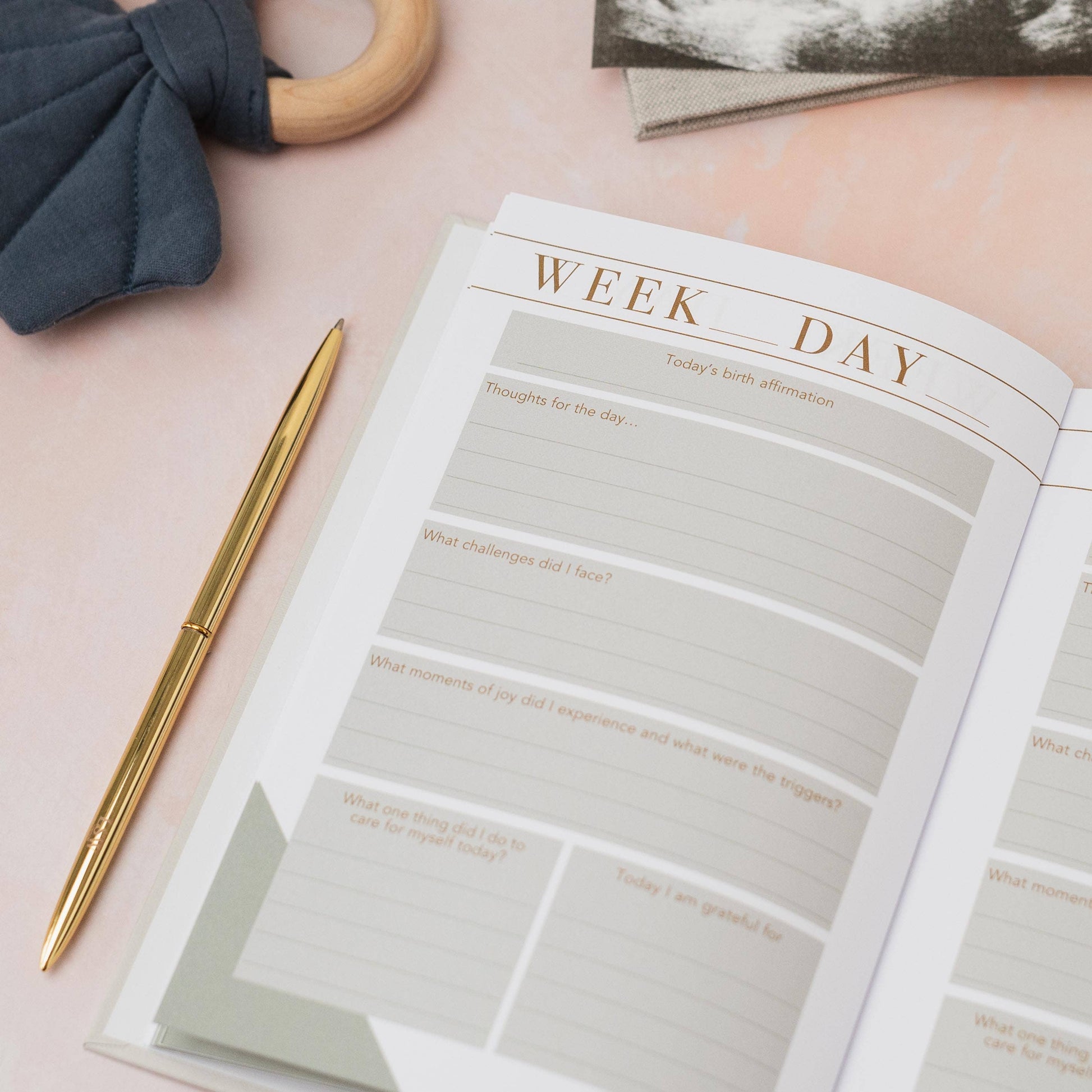 Open planner with daily reflection questions on a pink surface with a pen and decorative item.