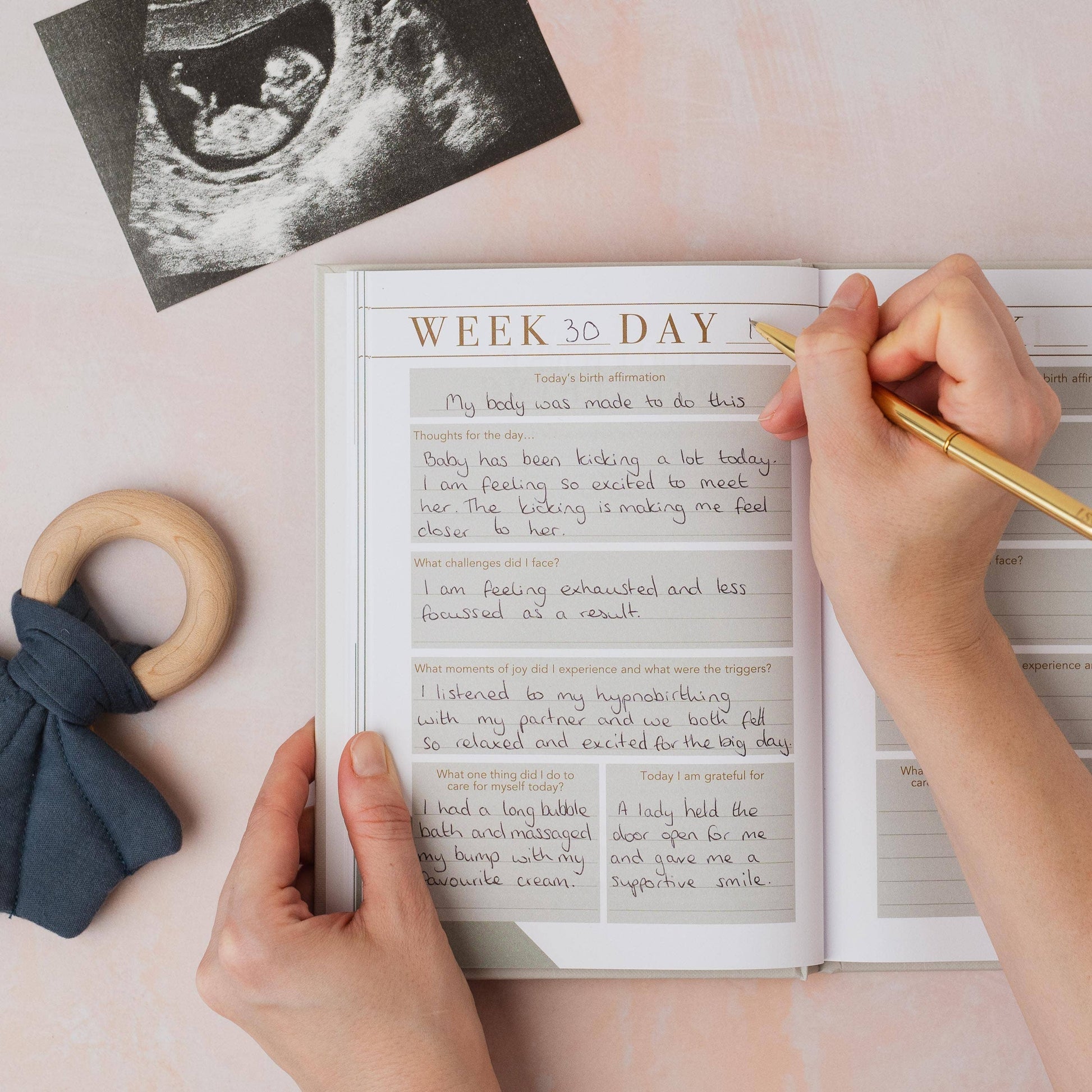 Person writing in a journal with an ultrasound photo and baby items on a light surface
