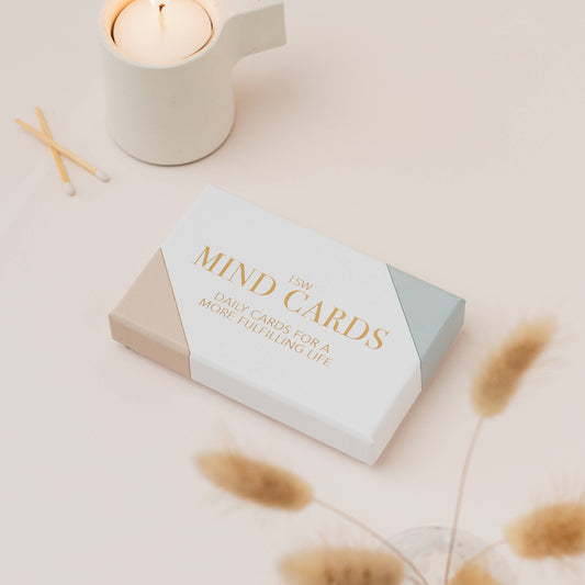Box of 'MIND GARDS' by LSW daily cards for a more fulfilling life on a light surface with a candle and dried plants.