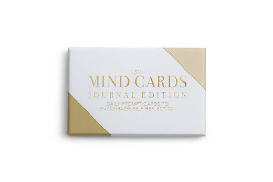 A packaged product labeled 'MIND CARDS JOURNAL EDITION' with a design predominantly in white and gold colors, indicating a collection of daily writing prompts for self-reflection.