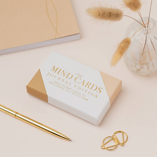 Box of 'Mind Cards Journal Edition' with a gold pen and decorative elements on a light background