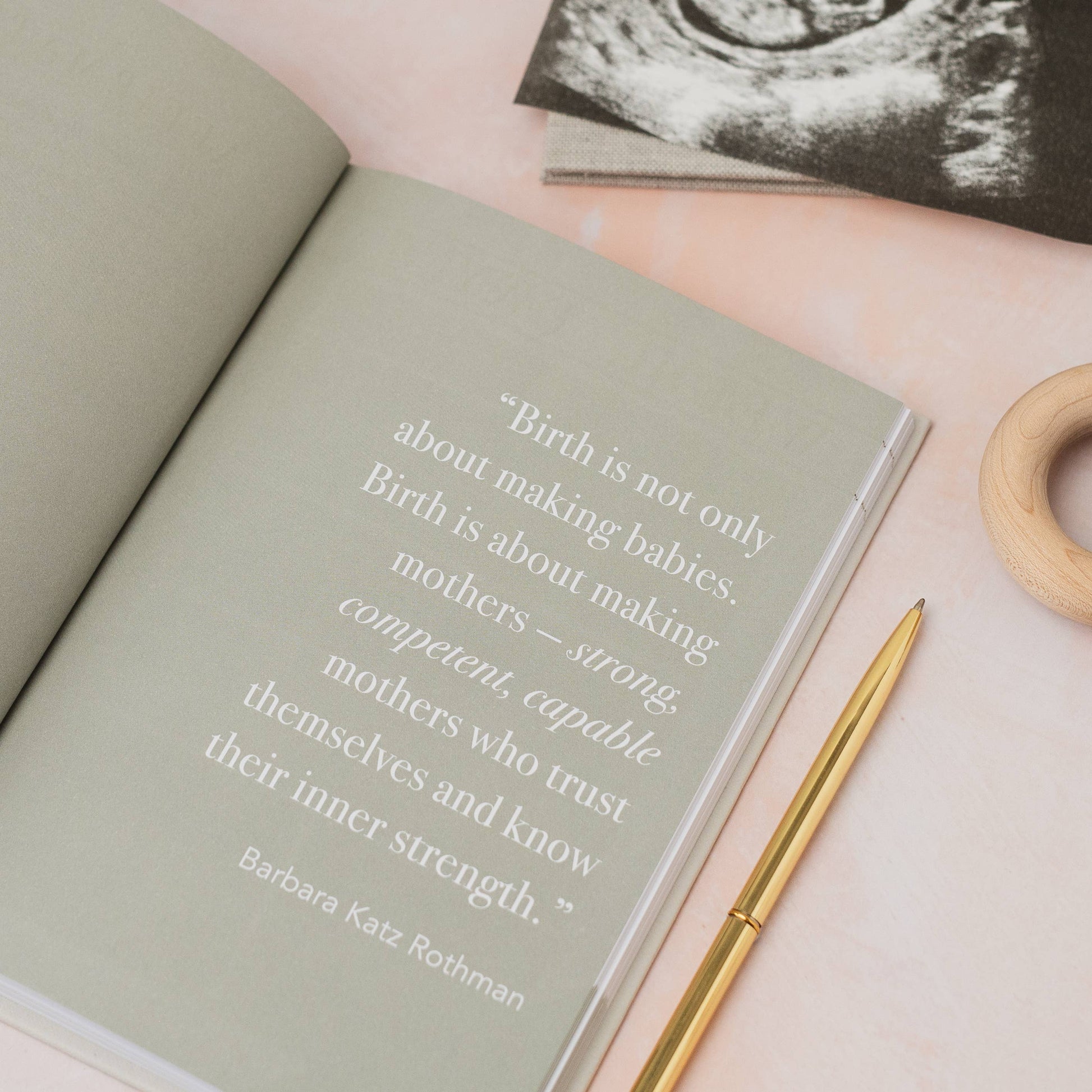 Open book with a quote on a pink surface with an ultrasound image and wooden ring.