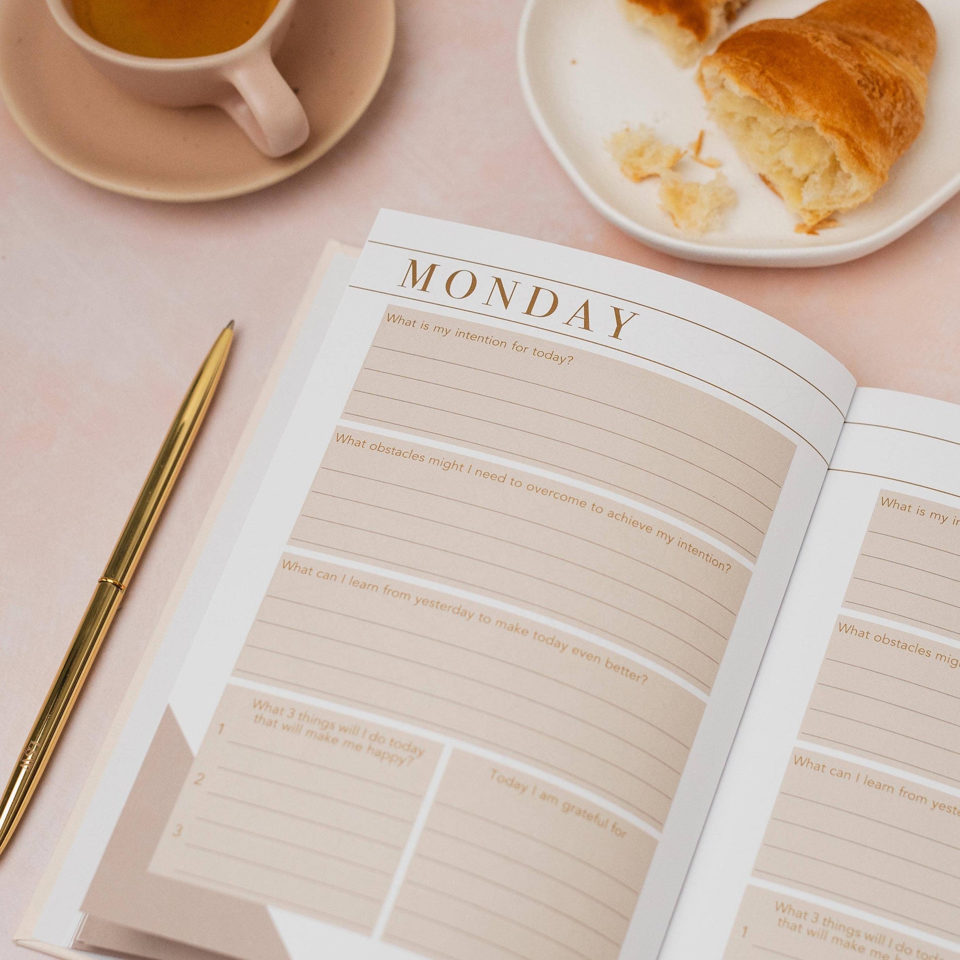 Open planner with a cup of tea and pastries on a pink surface