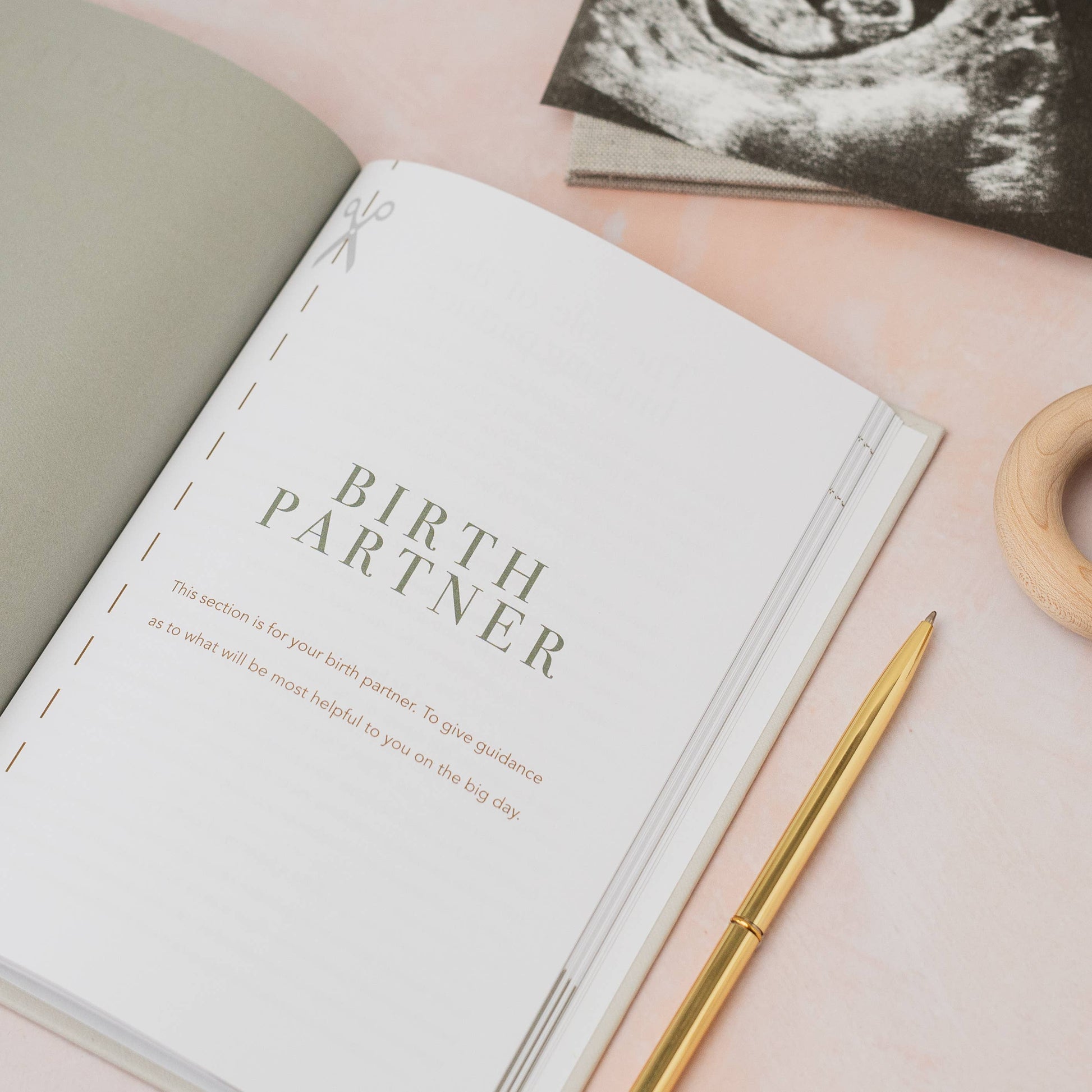 Open book titled 'Birth Partner' with a pen on a pink surface, ultrasound image in the background