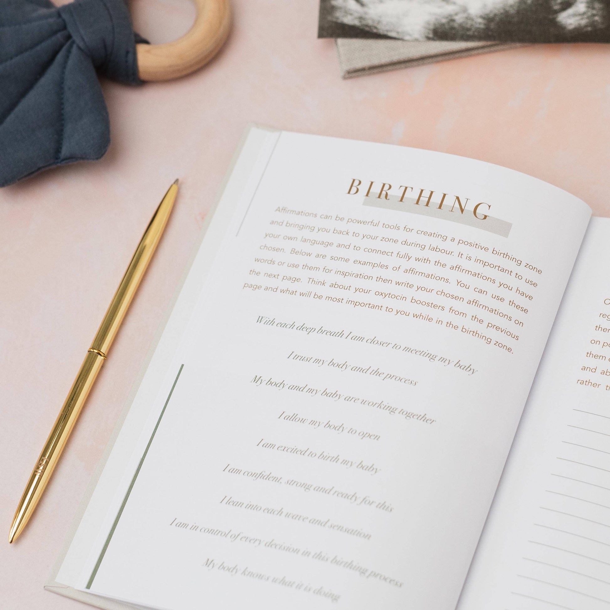 Open book with 'Birthing' text on a pink surface with a pen and blue fabric.