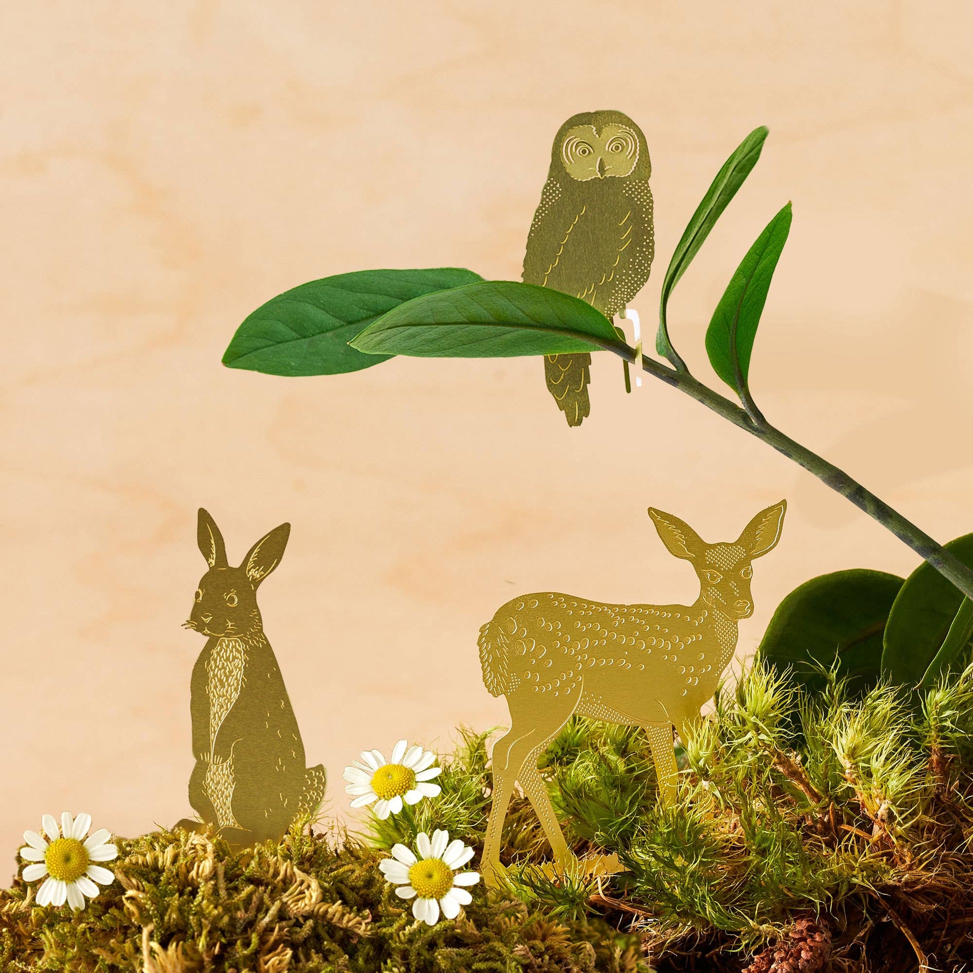A brass deer decoration placed on a plant pot, with green leaves in the background by Another Studio