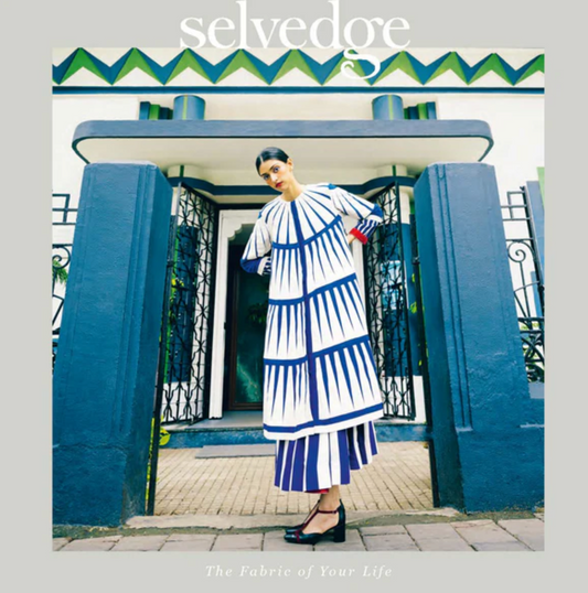 Woman in a blue and white dress standing in front of a decorative building entrance with 'selvedge' branding. Selvedge Magazine for Heart Gallery