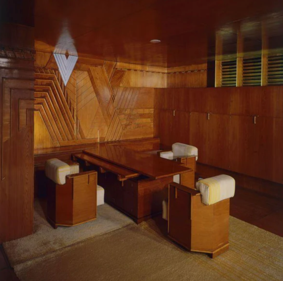 Wooden interior with a table and chairs in a room with geometric wall design.