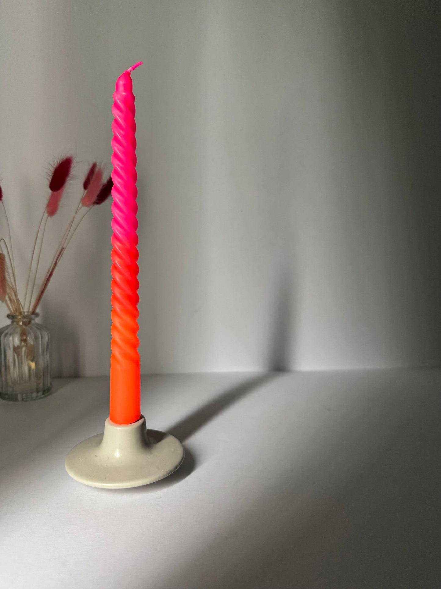 Neon pink and orange candle on a white base against a gray background
