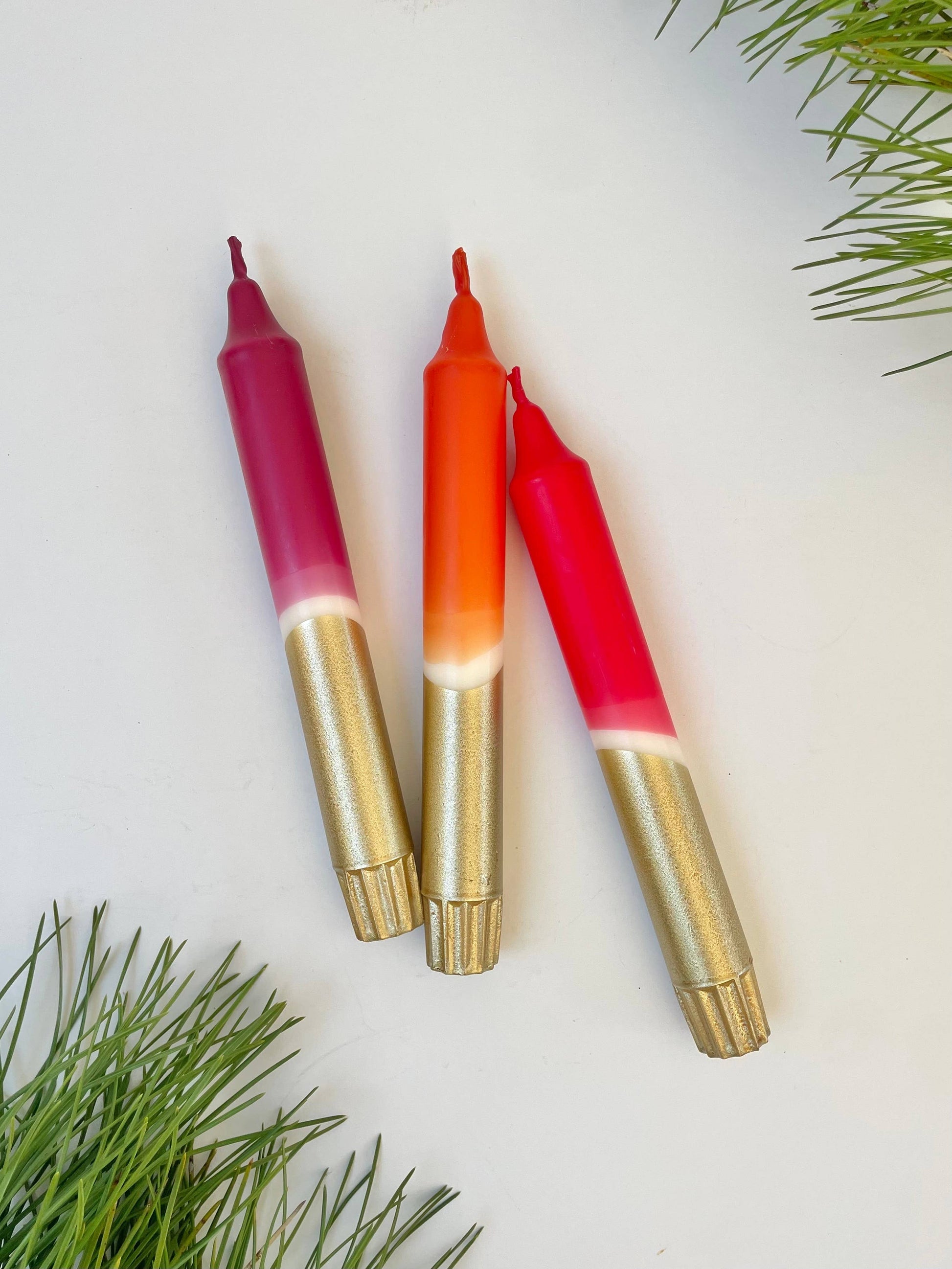 Three dip dyed gingerbread and gold candles on a light background with greenery.