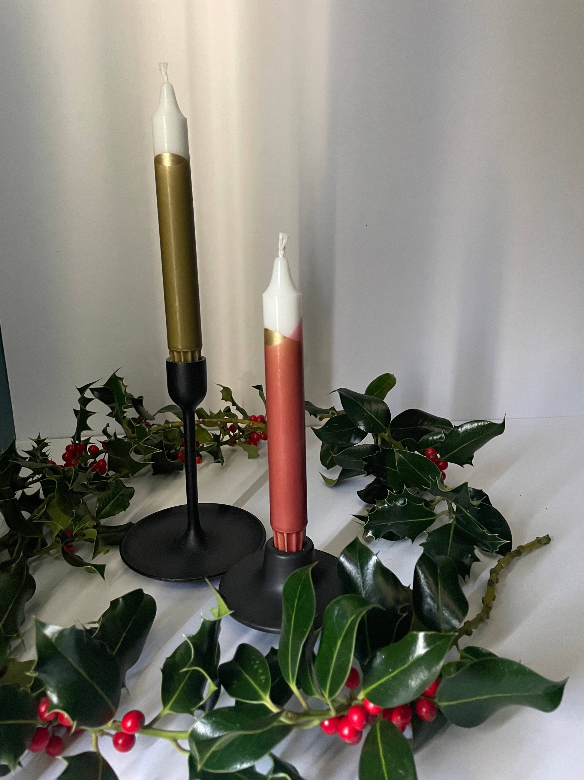 Decorative candles with gold and red accents on a white surface with green foliage.