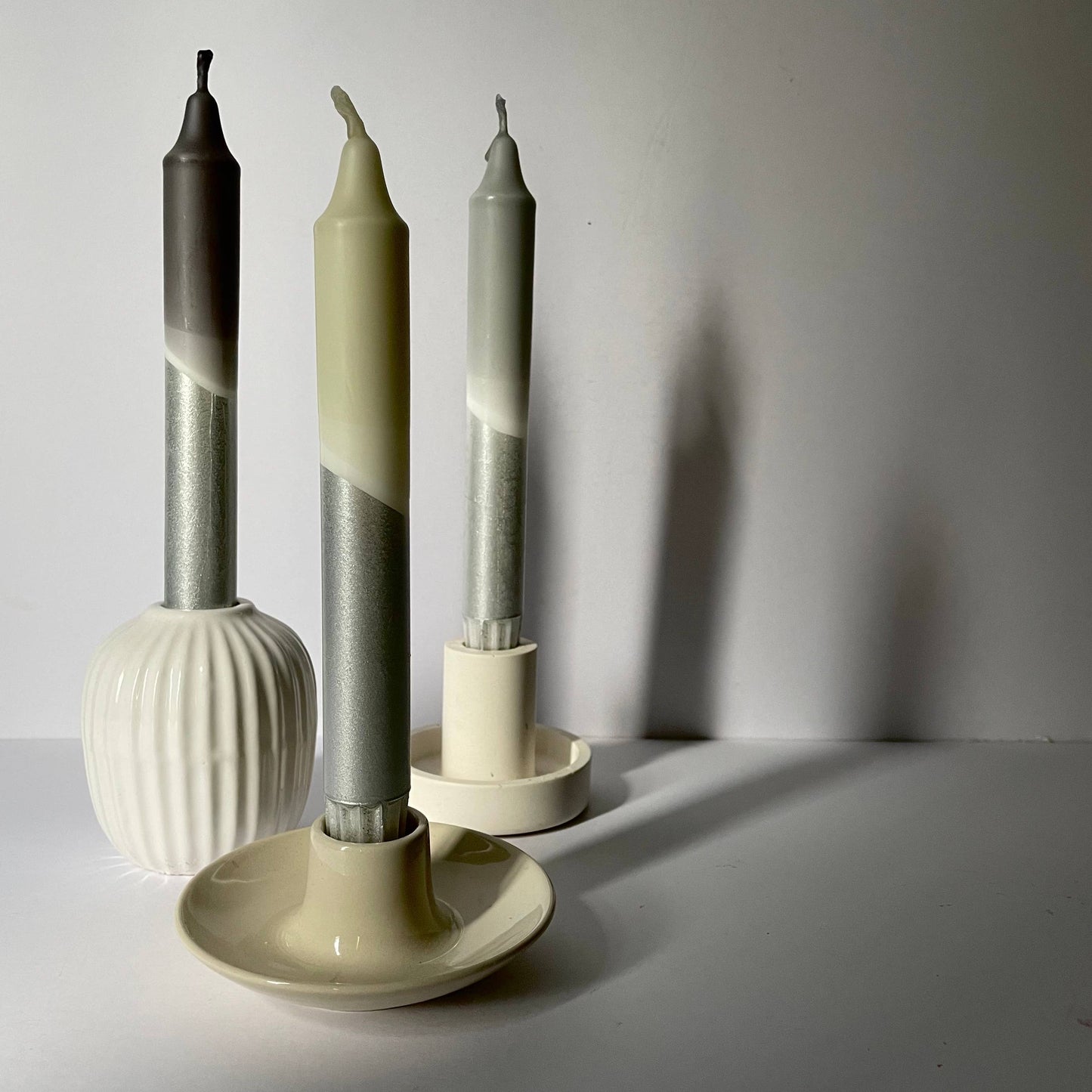 Three cylindrical candles with gradient colors in a white holder on a light gray background