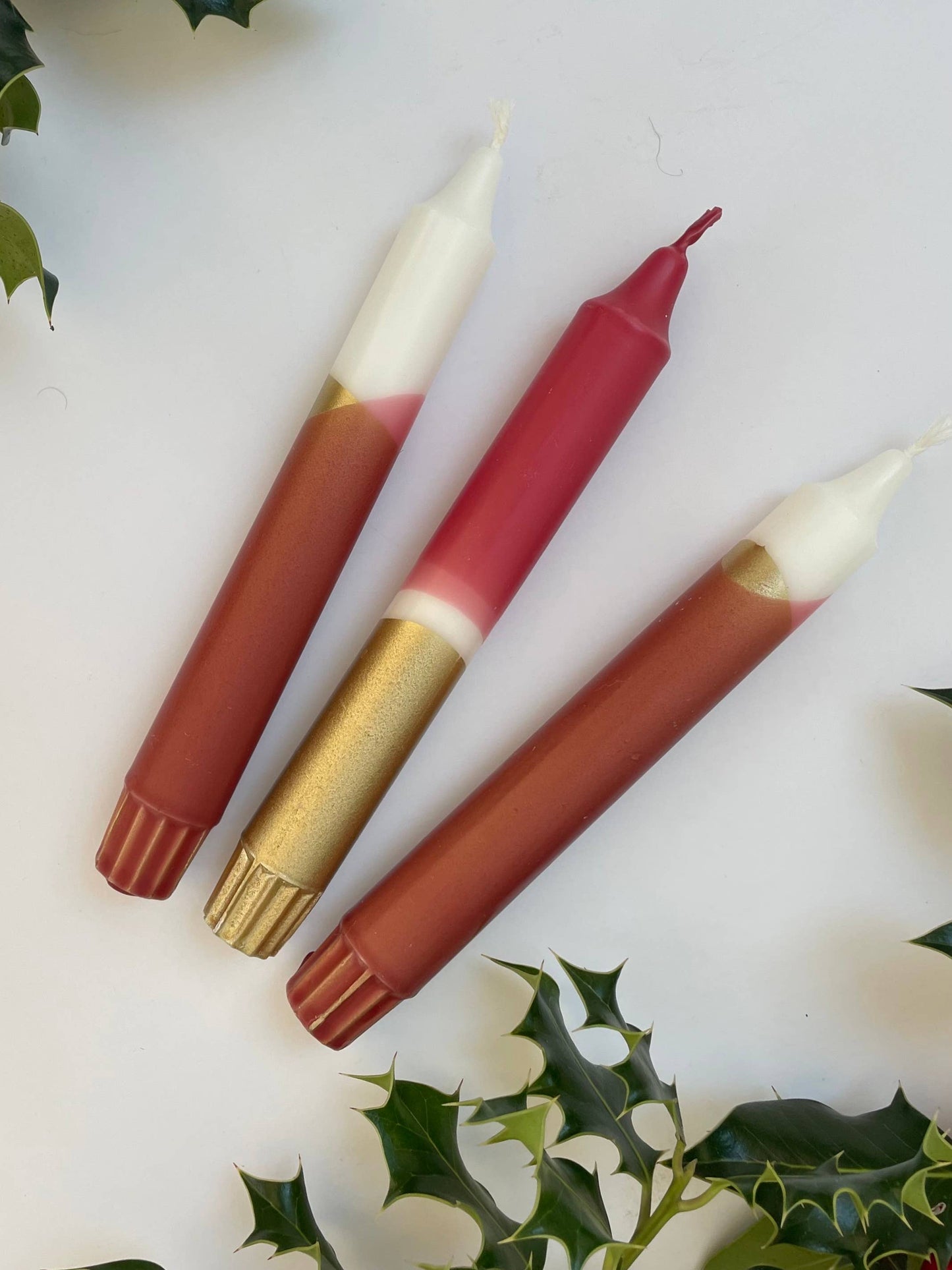 Three candles with different shades on a white background with holly leaves.