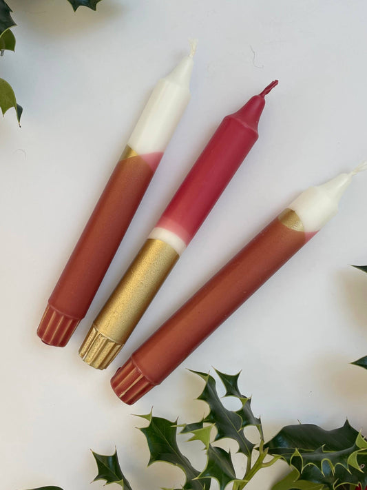 Three candles with different shades on a white background with holly leaves.